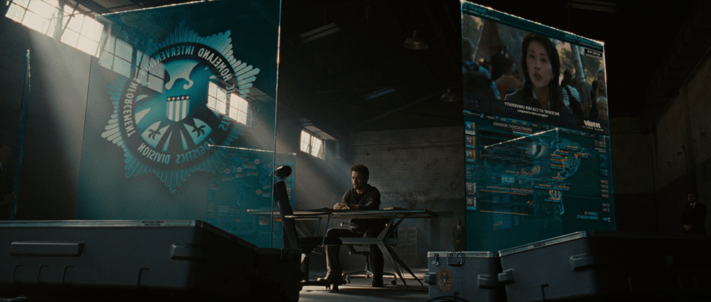 Tony Stark in a warehouse surrounded by S.H.I.E.L.D. information displays.
